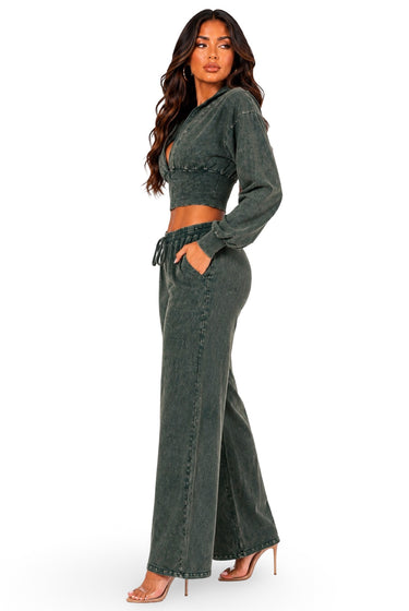 A woman modeling a matching two-piece outfit consisting of a dark gray-green long-sleeve crop top and high-waisted wide-leg pants, styled with clear high-heeled sandals against a plain white background.