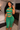 A woman takes a mirror selfie in a bedroom wearing a matching green ribbed two-piece set with a halter crop top and high-waisted leggings featuring horizontal cutouts.