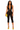 Angled front pose of black lace halter capri romper with deep V front, capri length, neon yellow heels, and matching clutch.