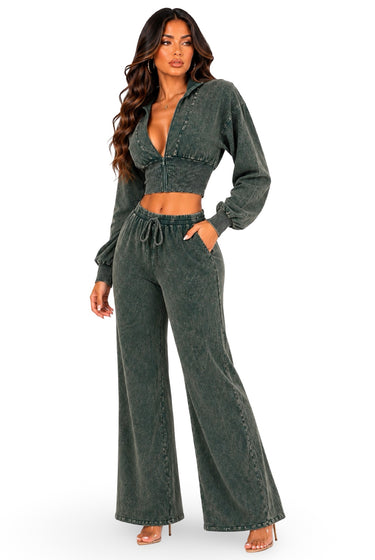 A woman modeling a matching two-piece outfit consisting of a dark green acid-wash long-sleeve crop top and matching wide-leg drawstring pants, set against a plain white background.