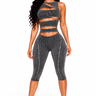 A woman modeling a matching two-piece activewear set in a washed charcoal gray color. The set includes a strappy cutout crop top and high-waisted cropped leggings with vertical seam detailing, shown against a plain white background.