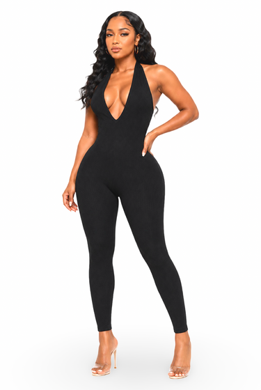 A woman modeling a black halter-neck, one-piece jumpsuit with a deep plunging neckline, photographed against a solid white background.