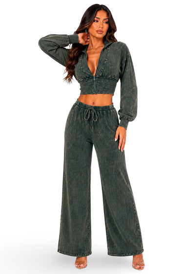 A woman modeling a matching two-piece outfit consisting of a dark washed green long-sleeve crop top with a front zipper and matching wide-leg drawstring pants, set against a plain white background.