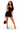 A woman modeling a fitted black halter mini dress with a square neckline, holding a small black handbag against a plain white studio background.
