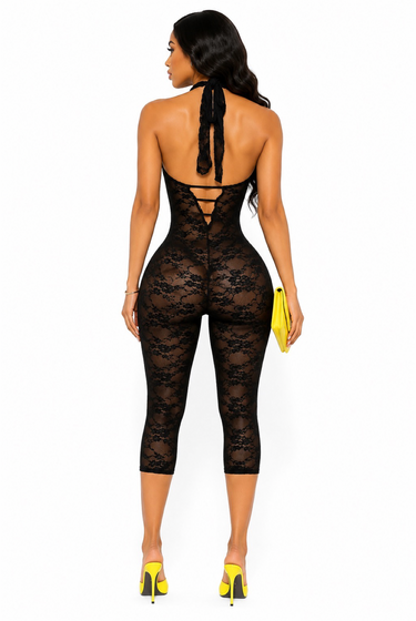 Back view of black halter lace capri romper featuring open back, tie neck detail, sheer floral lace, and bodycon silhouette.