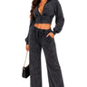 A woman modeling a dark gray acid-wash two-piece set consisting of a cropped zip-up hoodie and matching wide-leg drawstring pants, paired with clear high-heeled sandals and a small black handbag, against a plain white background.