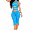 A woman modeling a bright blue two-piece activewear set consisting of a strappy cutout crop top and matching high-waisted capri leggings, set against a plain white background.