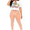 A woman modeling a white cropped graphic T-shirt with a cartoon print and a tied waist, paired with sheer nude high-waisted leggings and black high-heeled sandals, against a plain white studio background.